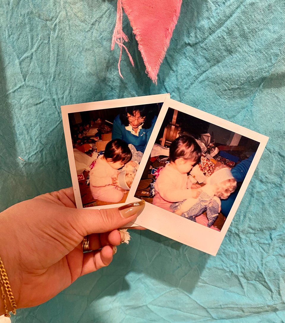 the hand of the artist holds two polaroid images with a baby holding a doll from different angles