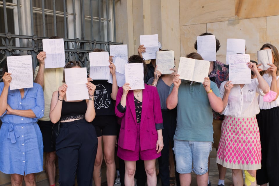 Tam photo of a previous Writing class; people holding their manuscripts in front of their faces