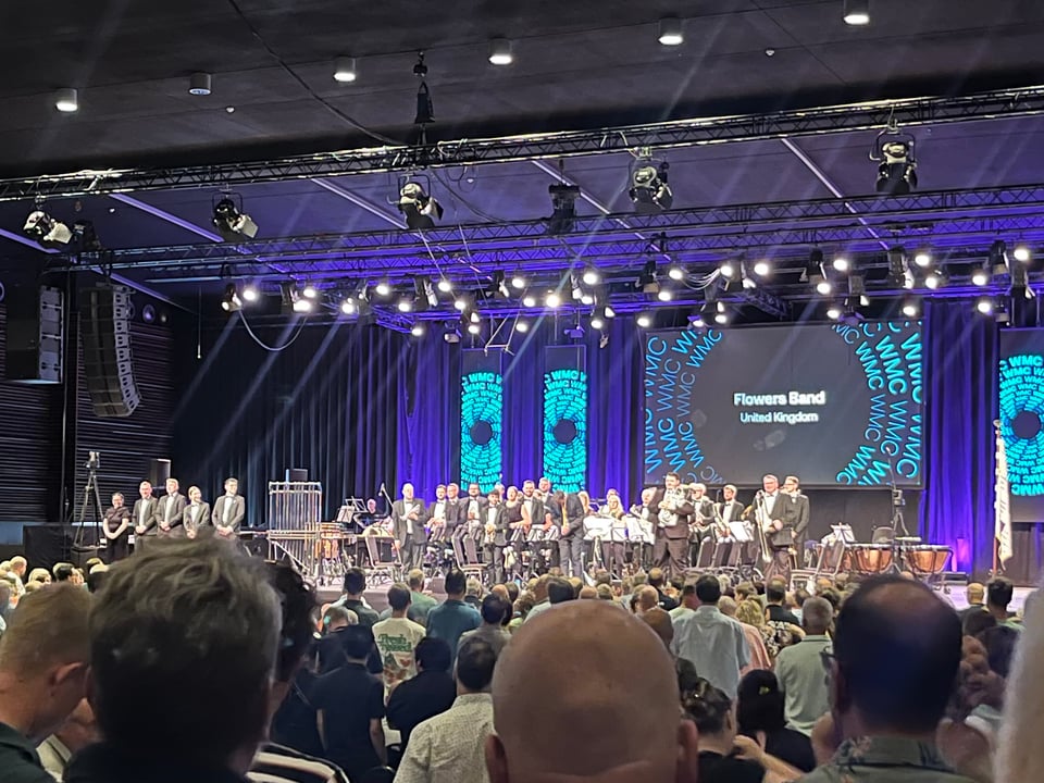 A blurry photo of Flowers Band standing on a stage, about to bow at the end of their second performance. Coco is on the far left with a group of five percussionists.