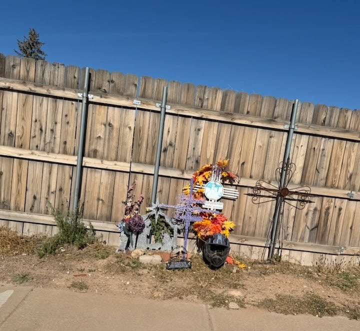 metal crosses, a pot, and many artificial flowers. wooden fence as backdrop.