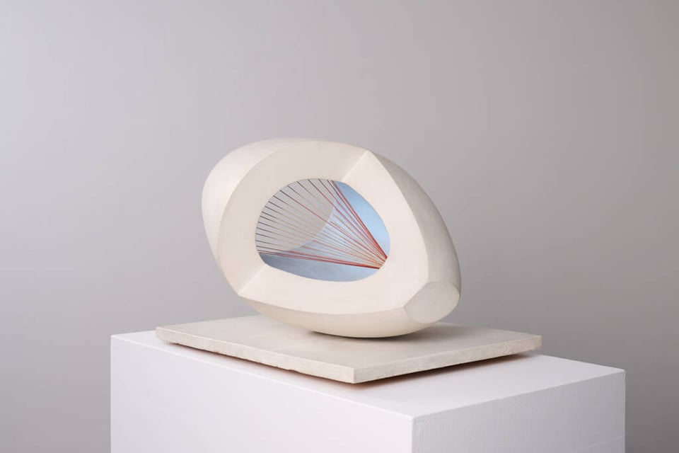 An ovoid sculpture with one corner cut away and a hole piercing it. The inside of the ovoid is duckshell blue and there are red strings running from a single point to the outer edges of the shape.