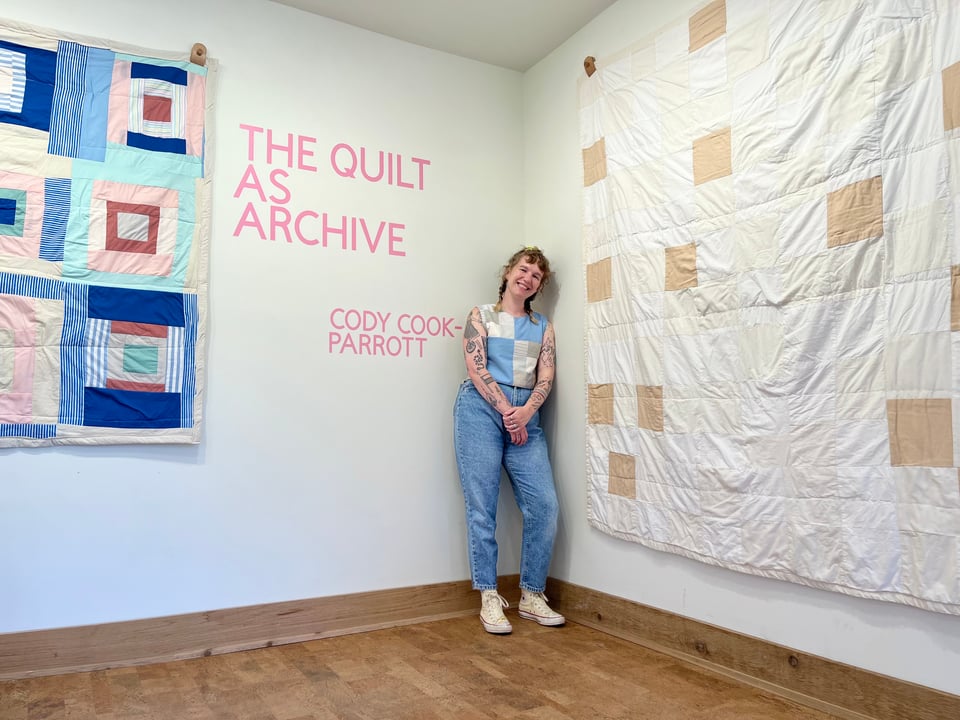 Cody standing in front of two colorful quilts
