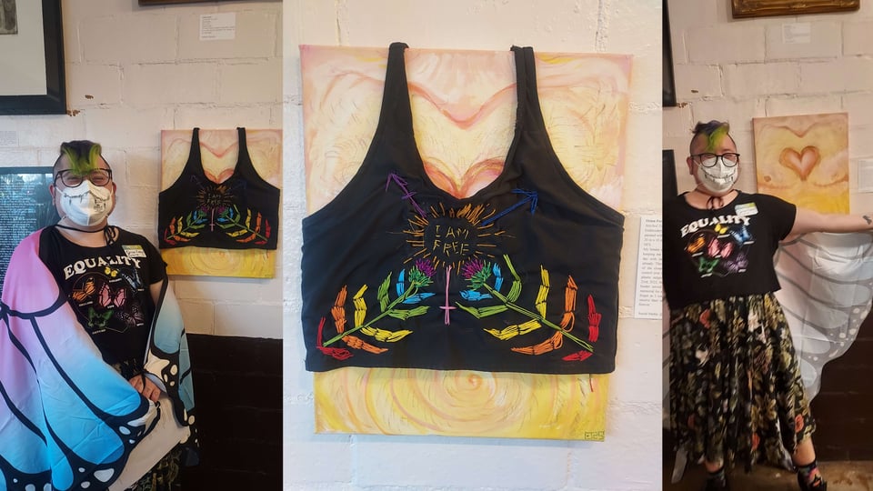 Me standing in my butterfly cloak and queer butterfly "Equality" t-shirt next to my canvas painting of my chest covered with a black binder, my actual old binder I used for a decade, that i embroidered to have "rainbow thistle plant scars" representative of the growth coming from top surgery. The trans symbol is crudely embroidered in with "I am free" inside of it. The photo has three shots, one of me standing with the binder version, the binder version in middle up close, and the removed binder bare post-op chest on the right with me spreading my butterfly cloak wings looking happy behind my N95 mask.