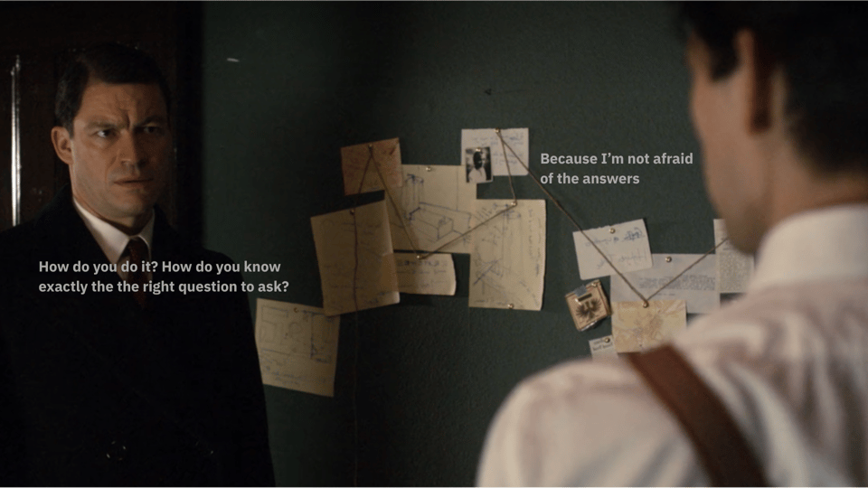 A still from the TV series The Hour. Two male actors face each other in front of a pinboard of ideas and story fragments. There are captions that tell us what they're saying. "How do you do it? How do you know exactly the right question to ask?" "Because I'm not afraid of the answers."