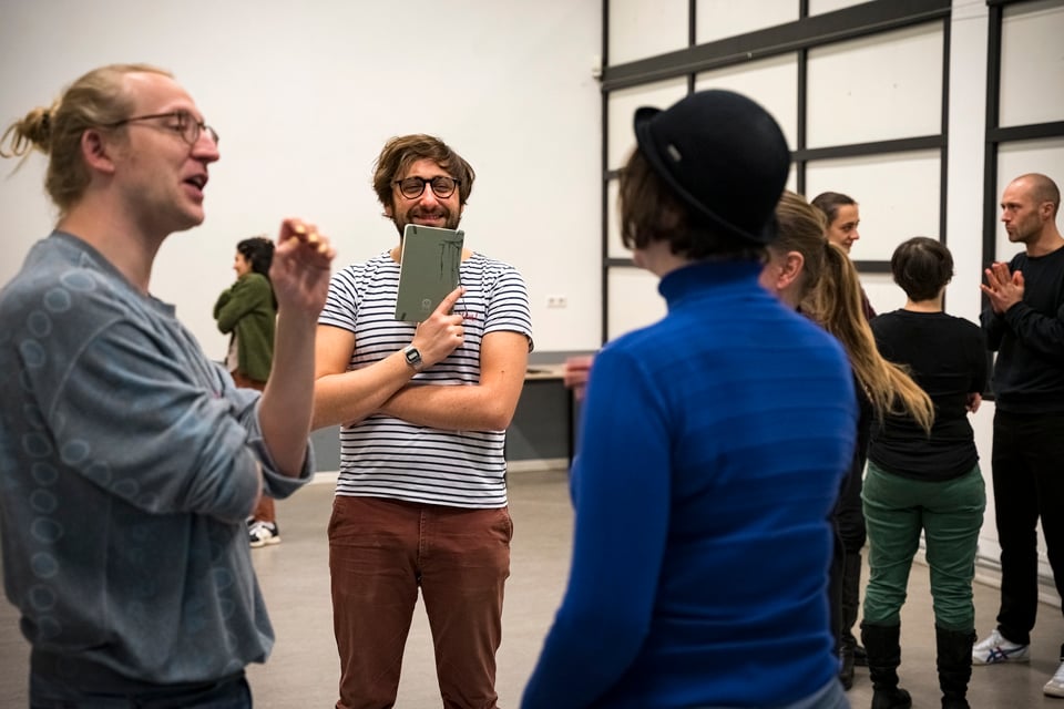 Gael teaching and holding a notebook, smiling while looking at a group of improvisers.