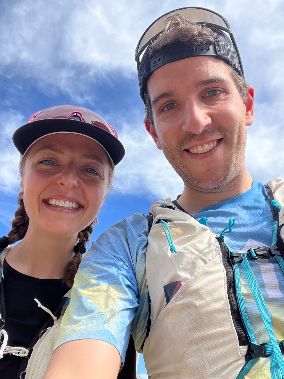 Adam and Kelsey in a selfie, wearing their running gear, before the Wharfbound Trail Races in Saint Andrews, NB. The sky is blue behind them and there is a small bank of clouds.