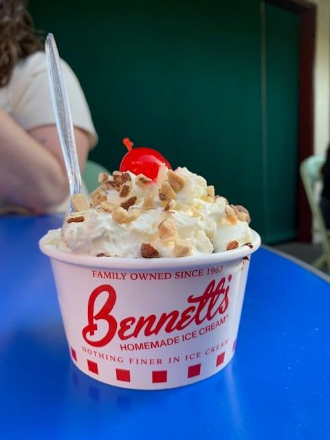 Whipped cream, nuts, and a cherry top an ice cream sundae in a paper cup that reads