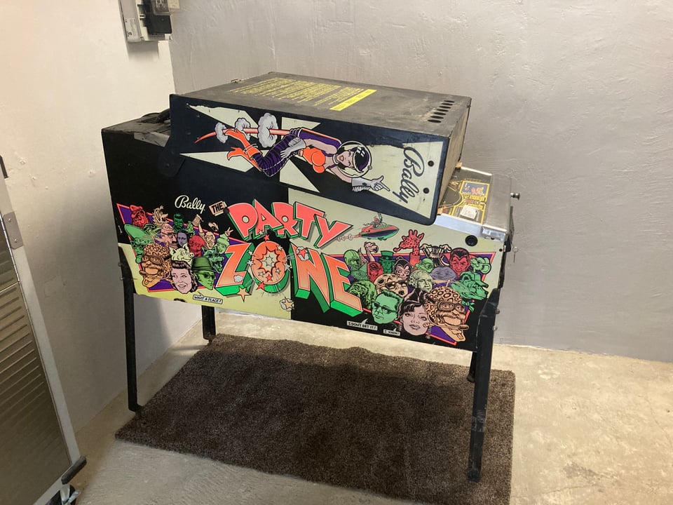 A "Party Zone" pinball machine with the backbox put down, standing in a garage.