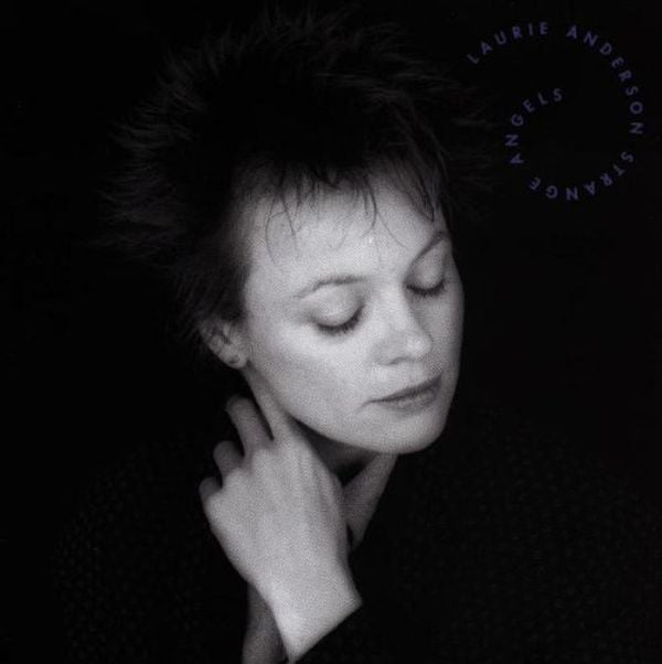 A black and white photo of Laurie Anderson, a white woman with short spiky dark hair. Her eyes are closed, her head titled at a slight angle to the left, and her hand is gently touching her throat.