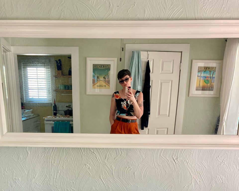 Mirror selfie of D. wearing a pair of orange pants and a black floral crop top.