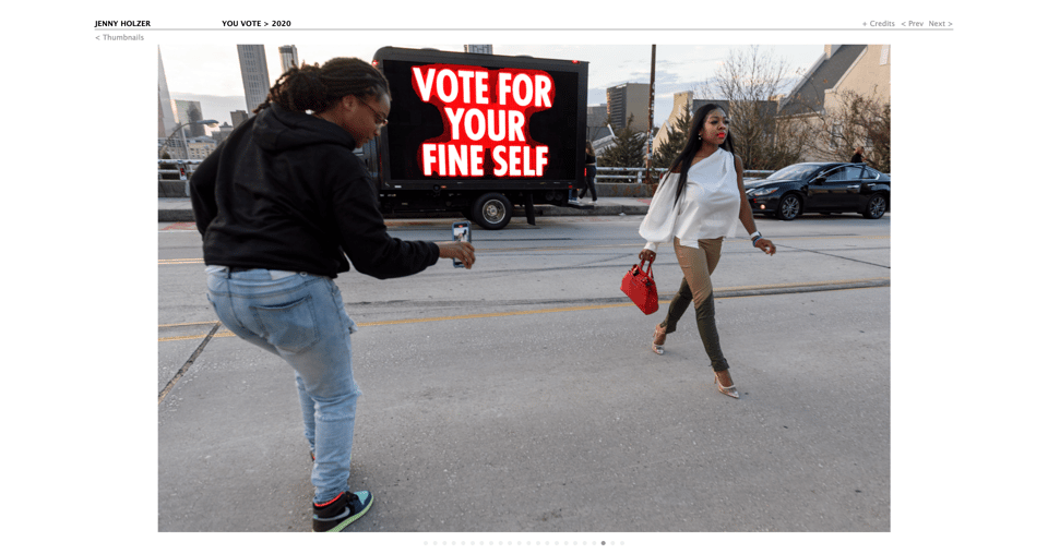 woman taking a stage photo for social media near a truck displaying the text Text: VOTE FOR YOUR FINE SELF