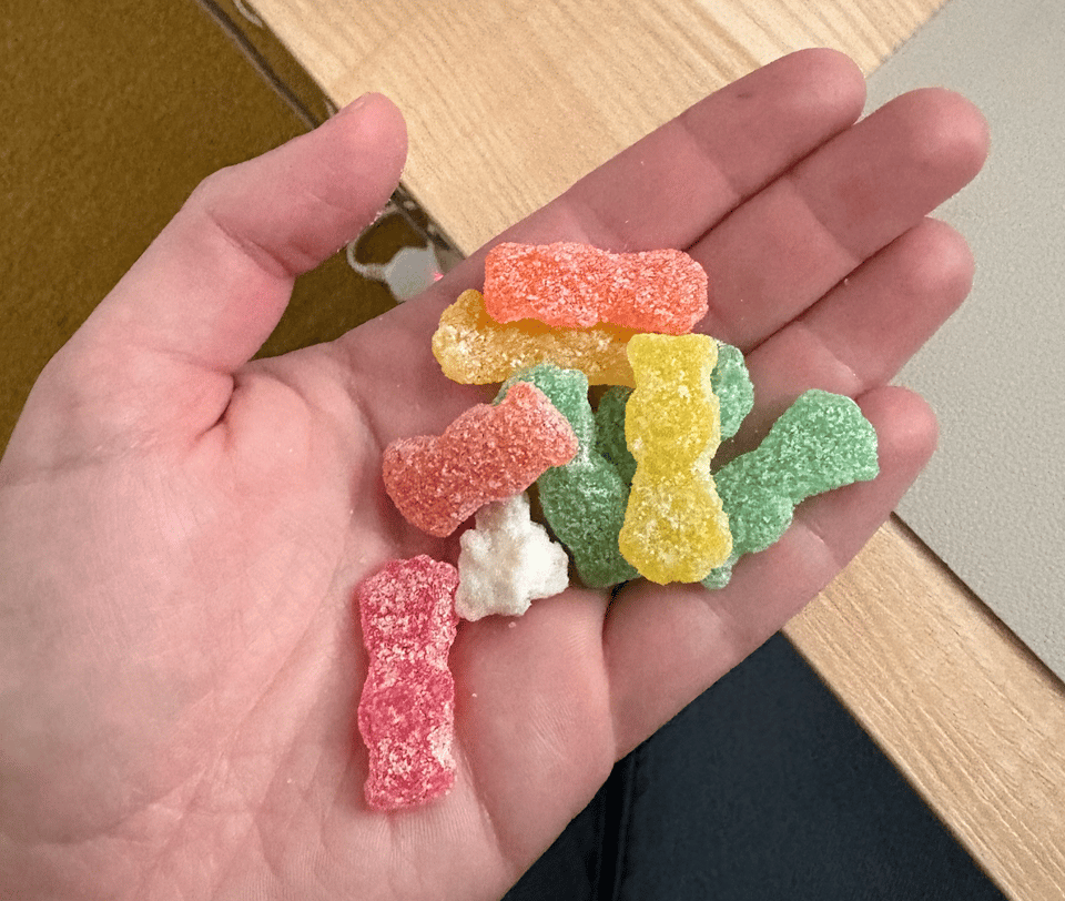 A hand holding Sour Patch Kids with one glob of all-white sour sugar looking like a rock in the middle