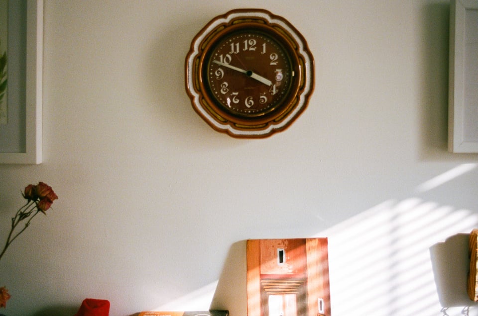 a cute vintage clock on a wall, striped with sunlight streaming through the blinds