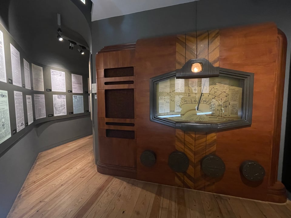 A hallway plastered with newspapers from the archives and an oversized sculpture of a wooden radio.
