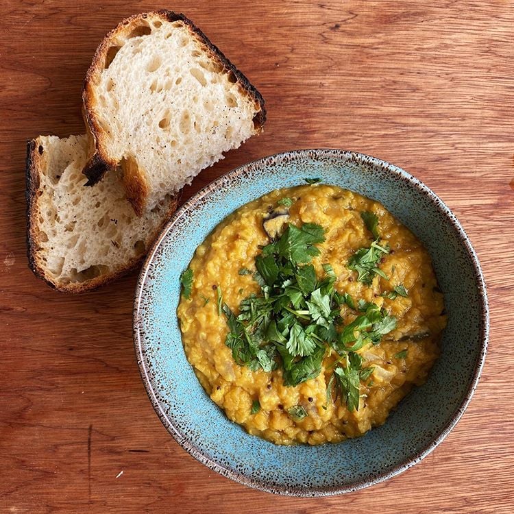 A bowl of Daal curry with a slice of sourdough bread, photographed from above.