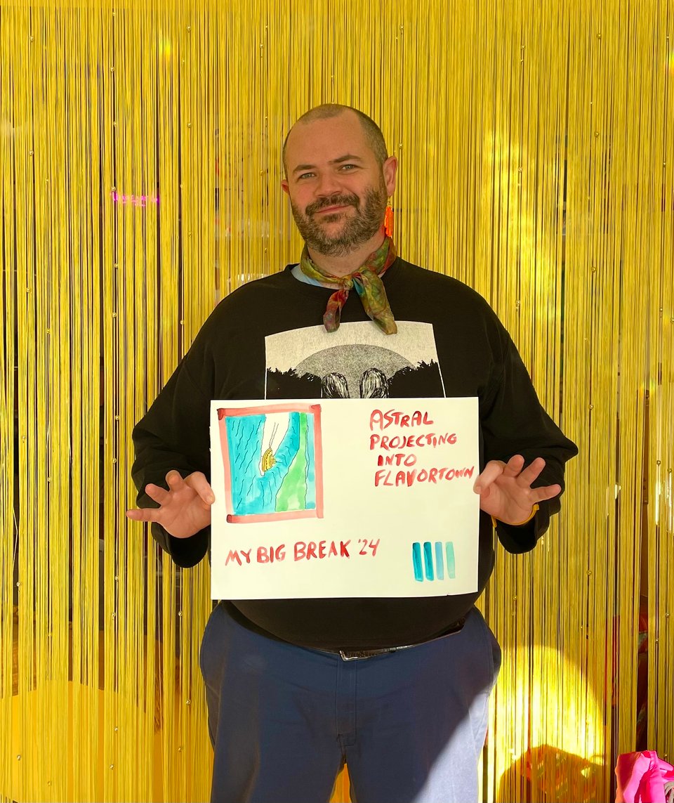 a man in a crewneck sweater stands before a curtain of yellow danglers holding a watercolor painting of a tugboat that reads "astral projecting into flavtortown"