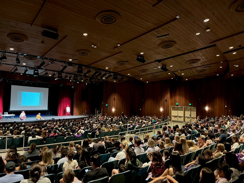 Photograph of Gale Galligan and Raina Telgemeier on stage during their book tour. They are presenting to an auditorium of kids and grownups.