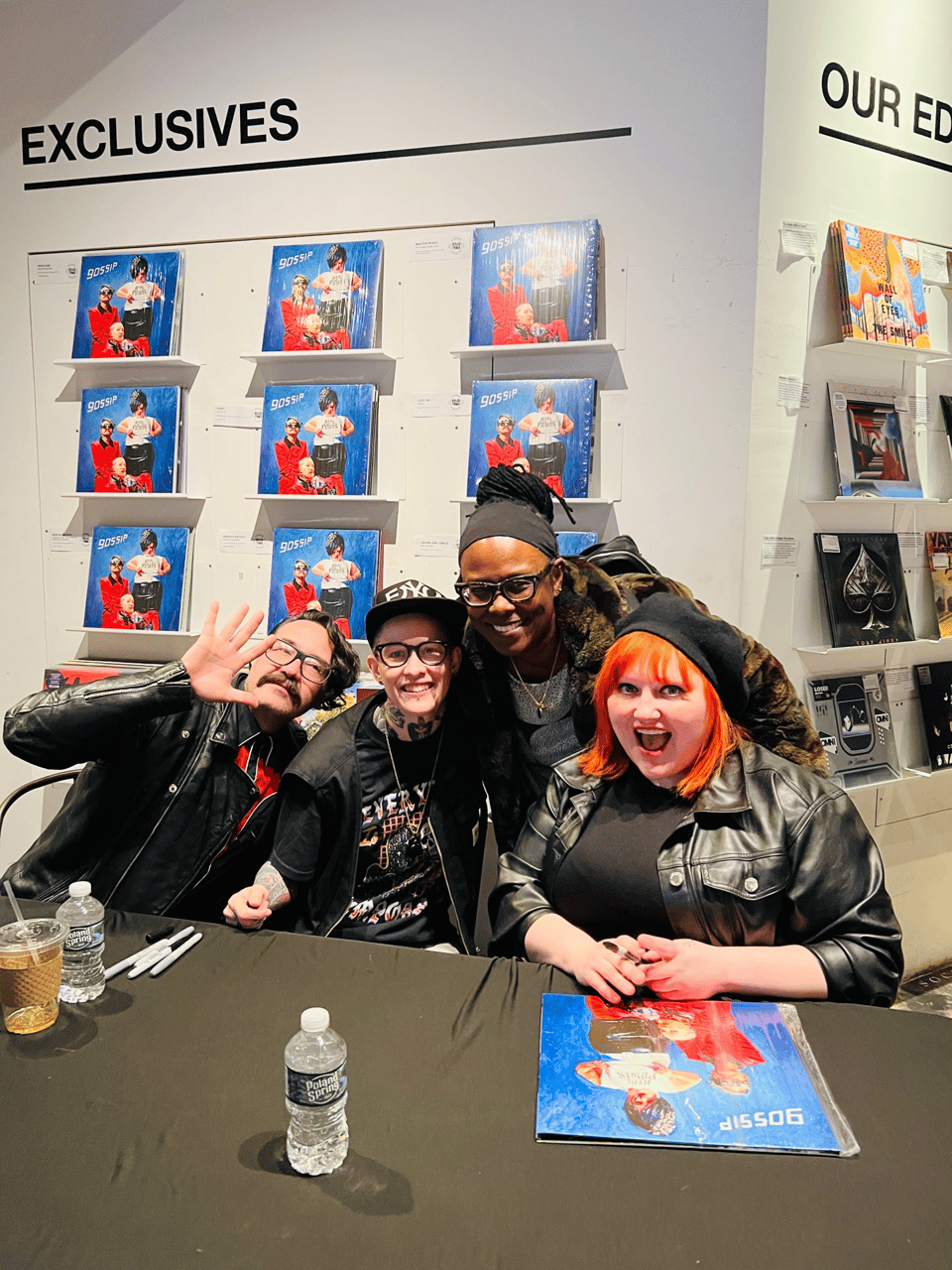 four people at a record signing smiling and waving