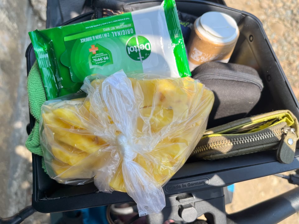 an image of an open bar bag attached to the handlebars of my touring bicycle in Sumatra, Indonesia, featuring a wallet, sunscreen, bag of pineapple slices and other everyday items