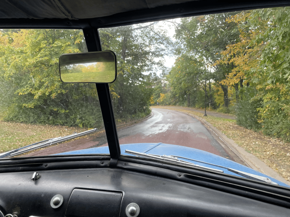 Looking out of the windshield of a 1950 panel truck down a curvy parkway road with trees' leaves just beginning to change color