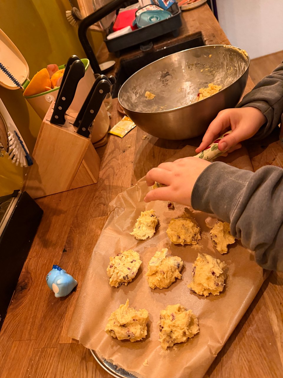 A young boy scoops out cookie dough onto a tray with parchment paper.