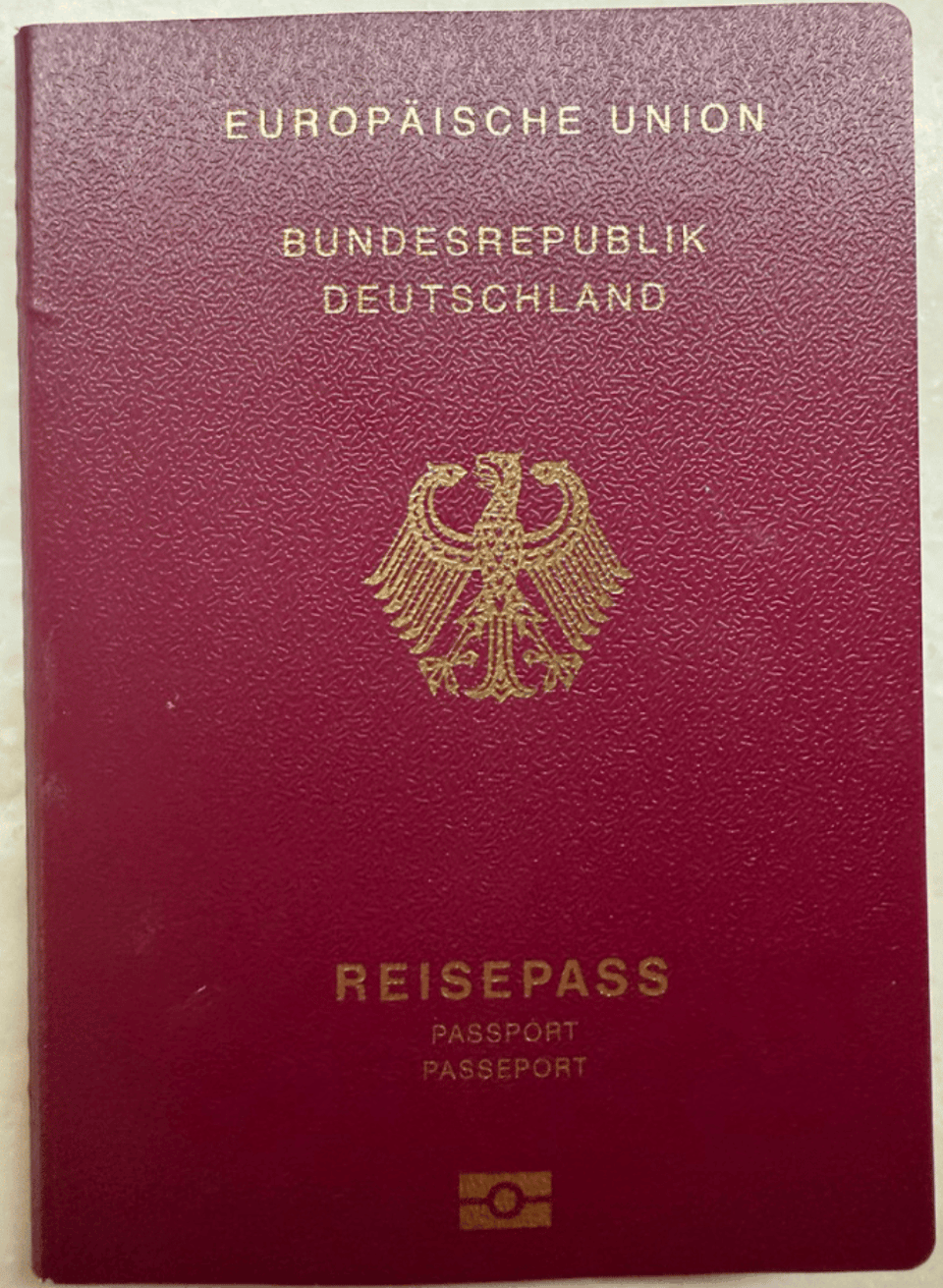 A maroon colored passport, with words and symbols in gold: EUROPAÏSCHE UNION, BUNDESREPUBLIK DEUTSCHLAND, REISEPASS, and in smaller letters PASSPORT AND PASSEPORT. In the middle is a stylized eagle with feathers, and at the bottom of the cover a rectangular icon that represents a biometric passport