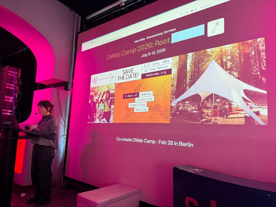 A woman stands at a podium in front of a presentation about DWeb unconference in Berlin on Feb 28.