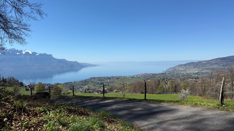 Landscape of a mountain road, with a village, a lake and snowy mountains in the background: Blonay in Switzerland.