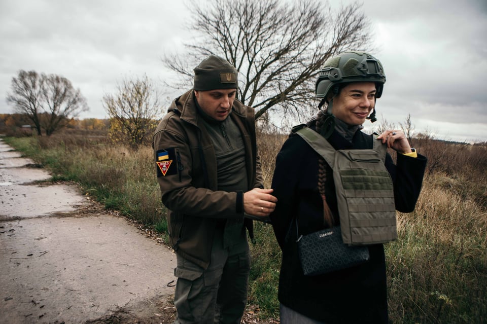 A male Ukrainian deminer helps a female Ukrainian deminer get dressed in PPE.