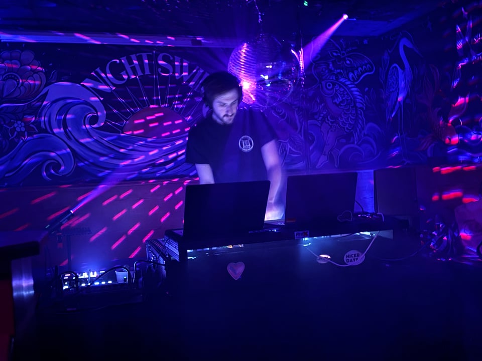 Evan bathed in blue and pink light, DJing on his birthday. A large disco ball is behind him.