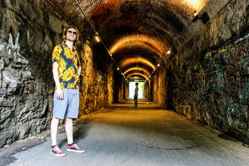 a photo of the electronic music duo Tall Glass in a tunnel. Evan stands triumphantly in the foreground, in a sunflower button down. Will (the writer of this email) is visible in the background, almost silhouetted.