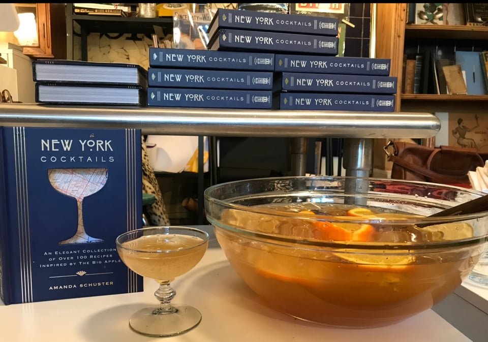 New York Cocktails book by Amanda Schuster on display at bookstore with glass of punch next to full punchbowl