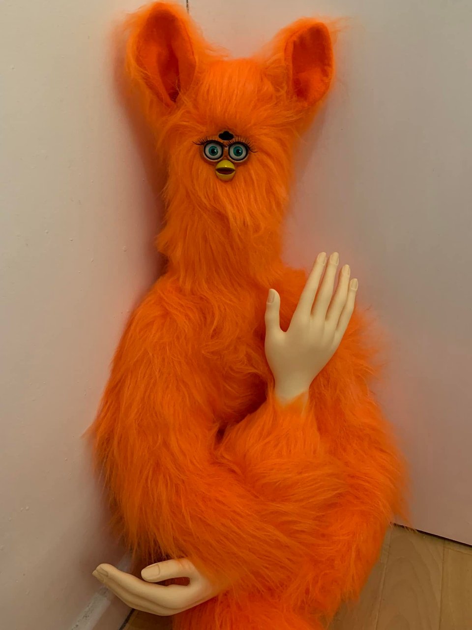 A bright orange Furby with human-like mannequin hands