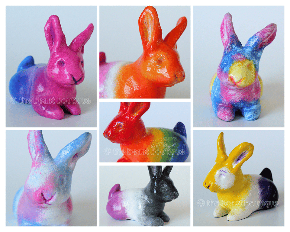 A collage showing different painted rabbit figurines in a loafing position from different angles. There are seven rabbits total, painted thusly: A bi pride rabbit, an ace pride rabbit, and a lesbian pride rabbit in a 3/4 view facing right, a pan pride rabbit and trans pride head on, and a rainbow rabbit and nonbinary pride rabbit facing 3/4 left.

the shop name, the beast boutique, watermarks the image.