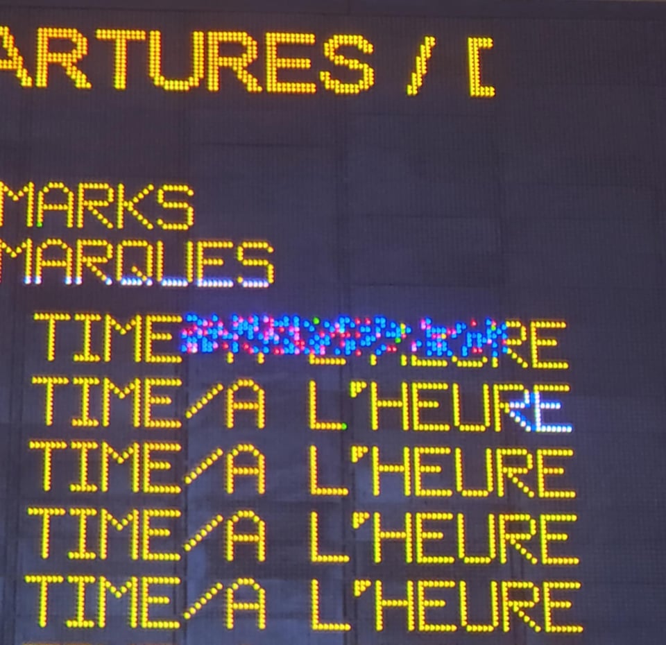 A train status board. Stray pixels corrupt the display. Lines of cut-off text read "Time / A L'Heure".