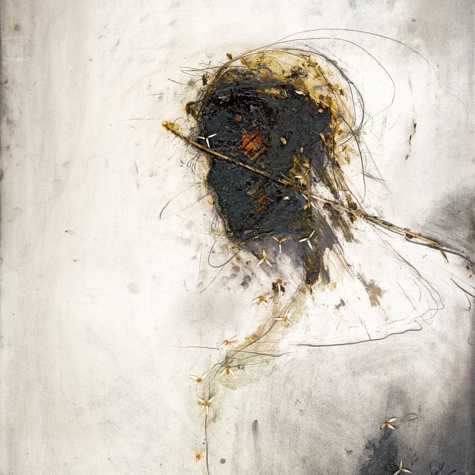 A really terrific mixed media portrait of (I presume) Jesus. On a white background with lots of dark smears (from coal?), is the outline of a figure, from the back up. The figure is turned away from us at an angle, but we get their profile. There are no details to the face; instead, the paper where the face has been outlined is black from ink, paint, coal, and maybe even burned a little bit. One spot where an eye would be is blot of red, probably paint but I'm not sure. There are tiny bits of flowers on the outline of the figure. There is a stick laid across the face of the figure that goes across their back as well. This could represent a whip, or possibly a crown of thorns? It's incredibly striking.