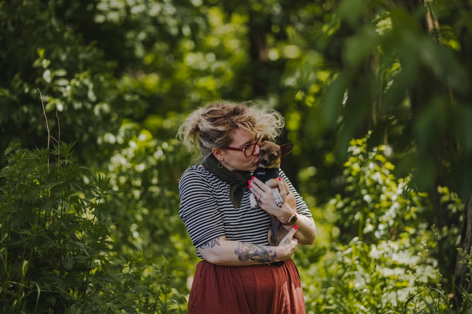 kate holding and kissing her dog, friday. they are surrounded by green leaves.