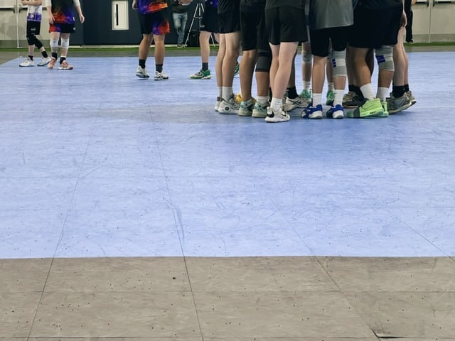A boys volleyball team huddled up before the game starts. Just their legs are visible.