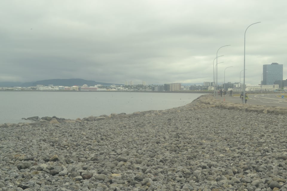 A stony beach under gray skies. Buildings can be seen on the other side of the bay, but are slightly shrouded in mist.