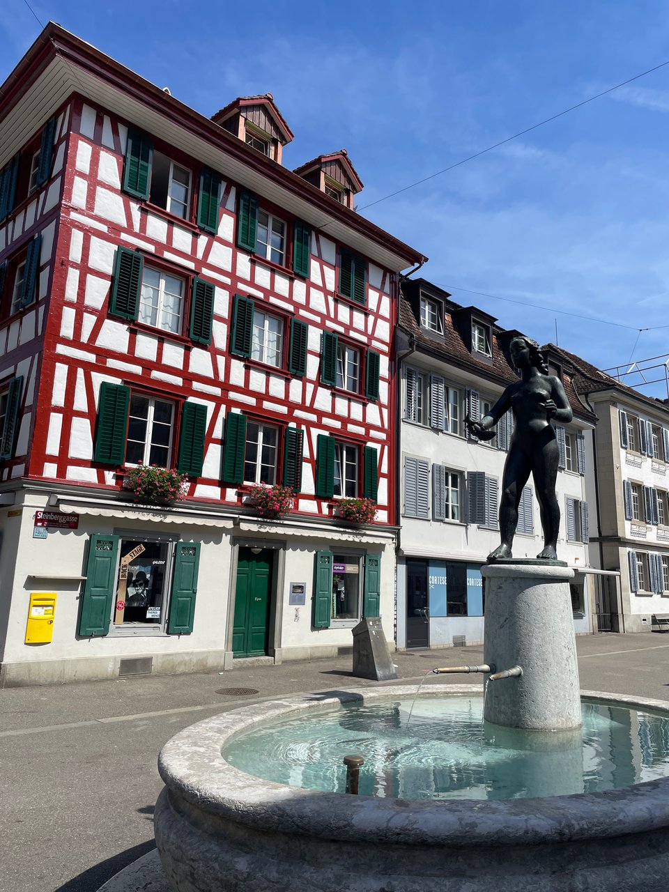 A fountain with a statue of a young girl holding a bird in the foreground, and swiss looking buildings in the background.
