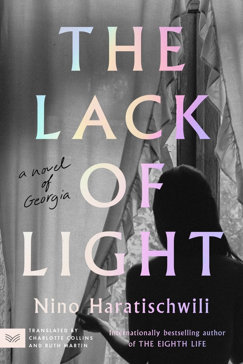 Black and white photo of a woman looking out a window, pushing aside curtain. Text over it, pale rainbow colors: THE LACK OF LIGHT / a novel of Georgia / Nino Haratischwili / TRANSLATED BY CHARLOTTE COLLINS AND RUTH MARTIN / Internationally bestselling author of THE EIGHTH LIFE