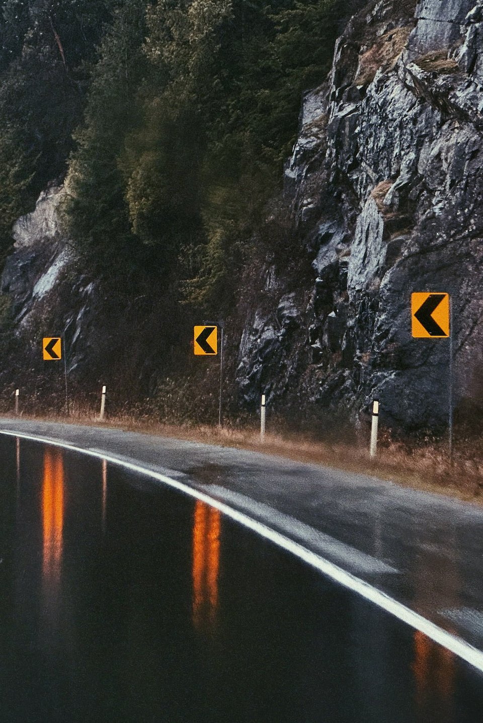 a bend in the road with yellow warning signs reflecting in the rain-laden asphalt