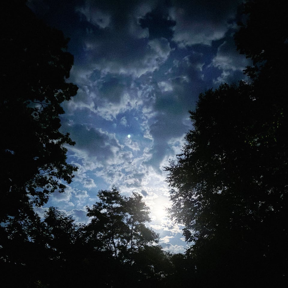 the strawberry moon absurdly bright in the sky obscured by clouds and seen from my driveway