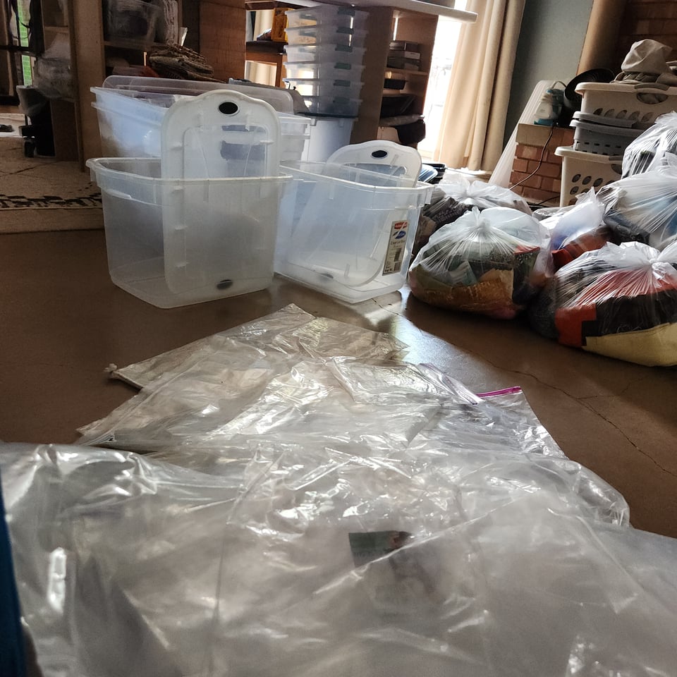Photo of Sarah's studio floor with a large pile of empty plastic bags, several empty plastic totes, and clear garbage bags full of discarded fabric.