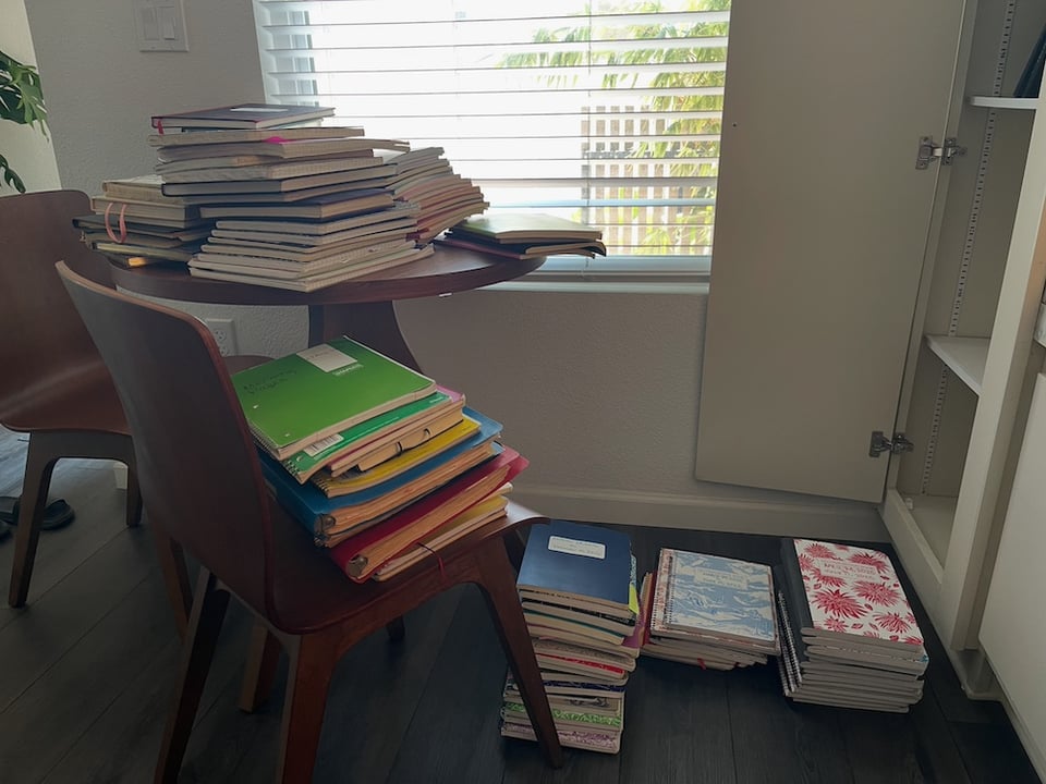 a chair and small round table as well as the floor are covered in stacks of notebooks