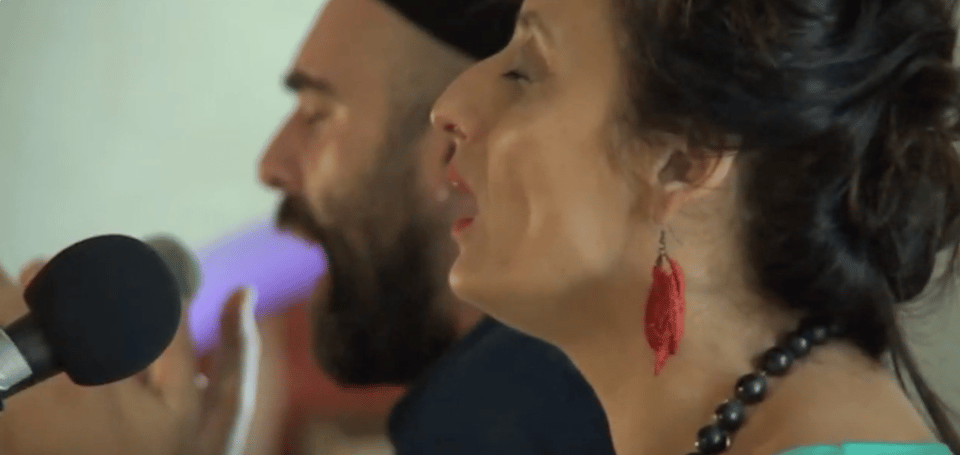 A close up of two faces singing into microphones, eyes closed.