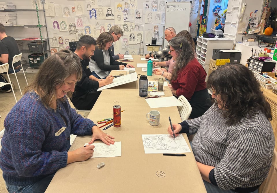 People drawing the person across from them at a long table