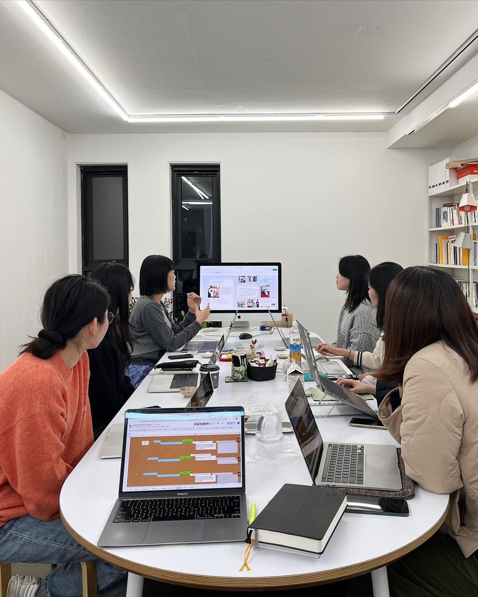 People sit around an oval table looking at a monitor while Suzin Kwone talks.