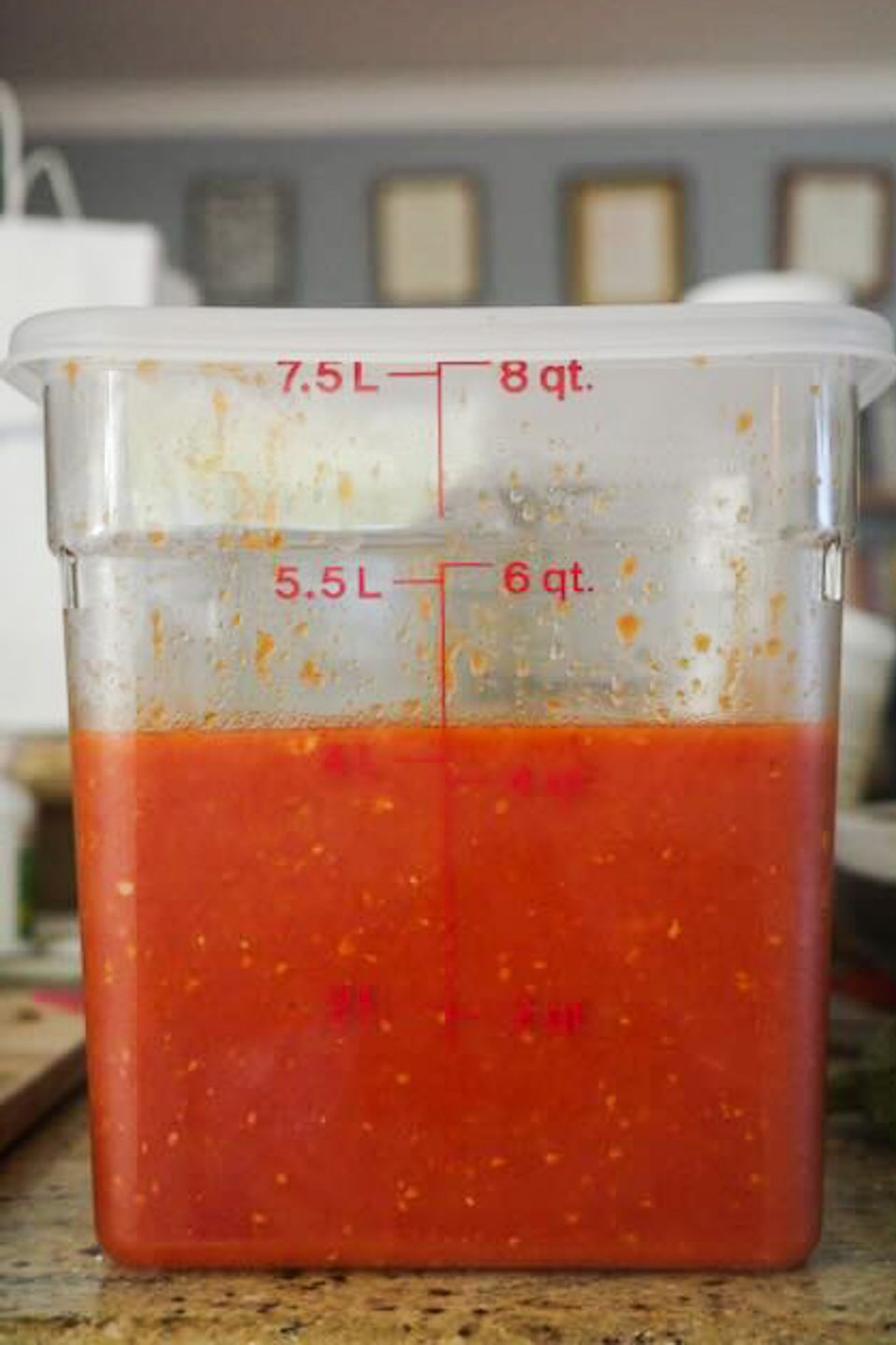 A square 7.5 liter cambro sits on a brown granite counter. It holds 4 liters of bright red tomato sauce