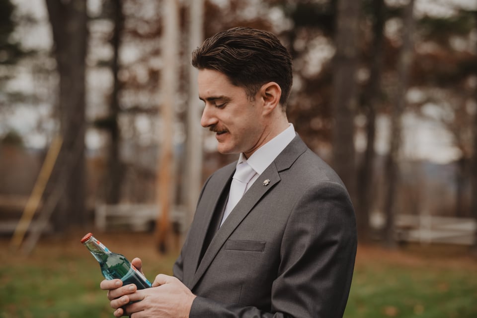 a man in a suit holding a bottle of smirnoff ice, he's about to chug the hell out of it